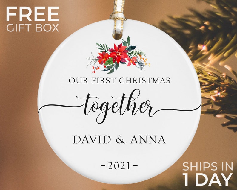 Puede incluir: Adorno navide&ntilde;o de cer&aacute;mica blanca con dise&ntilde;o floral y el texto "OUR FIRST CHRISTMAS together DAVID & ANNA -2021-". El adorno tiene una cinta dorada para colgar, una decoraci&oacute;n festiva.