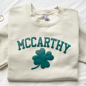 May include: A cream colored sweatshirt with a green shamrock and the text "MCCARTHY" in green.