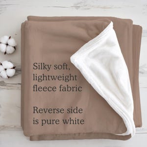 May include: A soft, lightweight fleece blanket in a warm brown color, with a pure white reverse side. The text on the blanket reads: "Silky soft, lightweight fleece fabric. Reverse side is pure white."