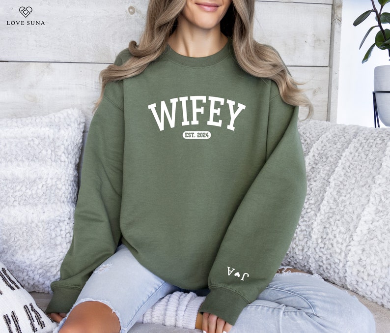 May include: A green sweatshirt with the text "WIFEY EST. 2024" in white. The sweatshirt has a white heart with an arrow on the left sleeve.