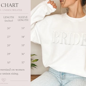 K&ouml;nnte beinhalten: Wei&szlig;er Unisex-Sweatshirt mit dem Wort "BRIDE" in erhabener Schrift. Die Gr&ouml;&szlig;entabelle zeigt die Ma&szlig;e in Zoll f&uuml;r die Gr&ouml;&szlig;en S, M, L, XL und 2XL.