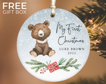 May include: A blue and white Christmas ornament with a brown bear illustration, a red gift box, and the text "My First Christmas Luke Brown 2022".