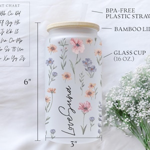 K&ouml;nnte beinhalten: Ein gefrosteter Glasbecher mit Bambusdeckel, verziert mit pastellfarbenen Blumen. Der Becher ist 15 cm hoch und 7,6 cm breit, mit dem Text "Love Suna". Enth&auml;lt einen BPA-freien Kunststoffstrohhalm.
