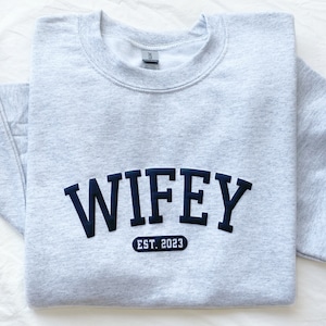May include: Grey sweatshirt with black text that reads "WIFEY EST. 2023".