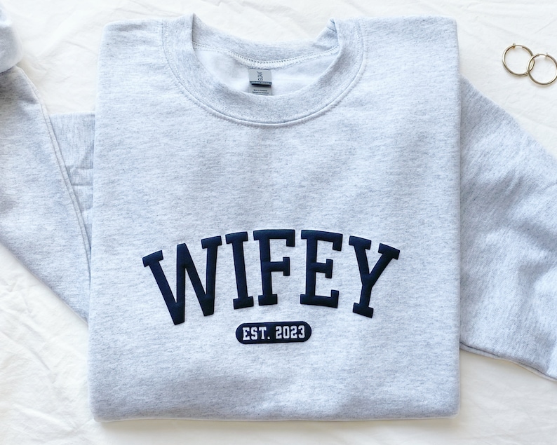 May include: Grey sweatshirt with black text that reads "WIFEY EST. 2023".