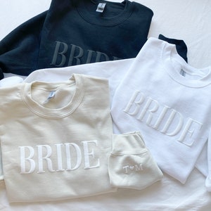 K&ouml;nnte beinhalten: Drei Sweatshirts mit dem Wort "BRIDE" bestickt. Die Sweatshirts sind in Schwarz, Wei&szlig; und Beige.