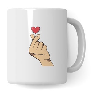 Può includere: Tazza in ceramica bianca con una mano che fa un gesto a forma di cuore con un cuore rosso sopra.
