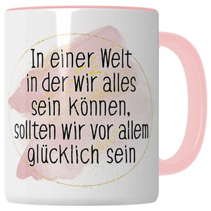 Può includere: Tazza in ceramica bianca con interno e manico rosa. La tazza presenta un design ad acquerello rosa con macchie dorate e testo nero che recita: "In einer Welt in der wir alles sein können, sollten wir vor allem glücklich sein."