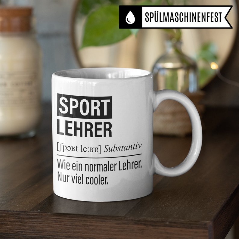 May include: White ceramic mug with a black design that says "SPORT LEHRER [sport le:ʁɐ] Substantiv Wie ein normaler Lehrer. Nur viel cooler."