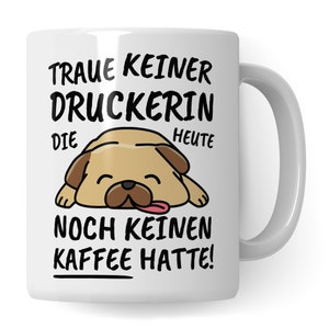 Op de afbeelding: Witte keramische mok met een cartoon-illustratie van een mopshond. De mok heeft zwarte tekst die luidt "Traue keiner Druckerin die heute noch keinen Kaffee hatte!"