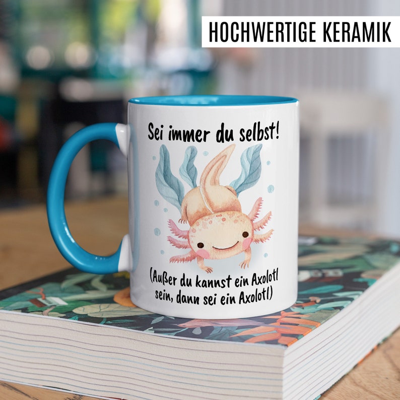 May include: White ceramic mug with a blue handle. The mug has a watercolor illustration of an axolotl with the text "Sei immer du selbst! (Au&szlig;er du kannst ein Axolotl sein, dann sei ein Axolotl)"