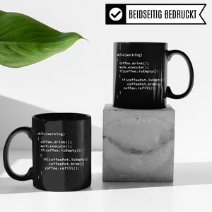 May include: Two black coffee mugs with white code printed on them. The code reads "while(working) { coffee.drink(); work.execute(); if(coffee.isEmpty()) { if(coffeePot.isEmpty()) coffeePot.brew(); coffee.refill(); } ". The text "BEIDSEITIG BEDRUCKT" is printed on the top of the mug on the right.
