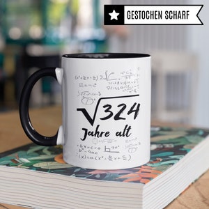 May include: White ceramic mug with a black handle. The mug has black text and mathematical equations printed on it. The text reads "&radic;324 Jahre alt".
