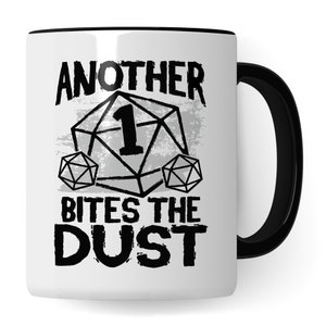 Könnte beinhalten: Weiße Keramiktasse mit schwarzem Rand und Henkel. Die Tasse zeigt eine schwarz-weiße Grafik eines Würfels mit der Zahl 1 darauf und dem Text "Another Bites The Dust".