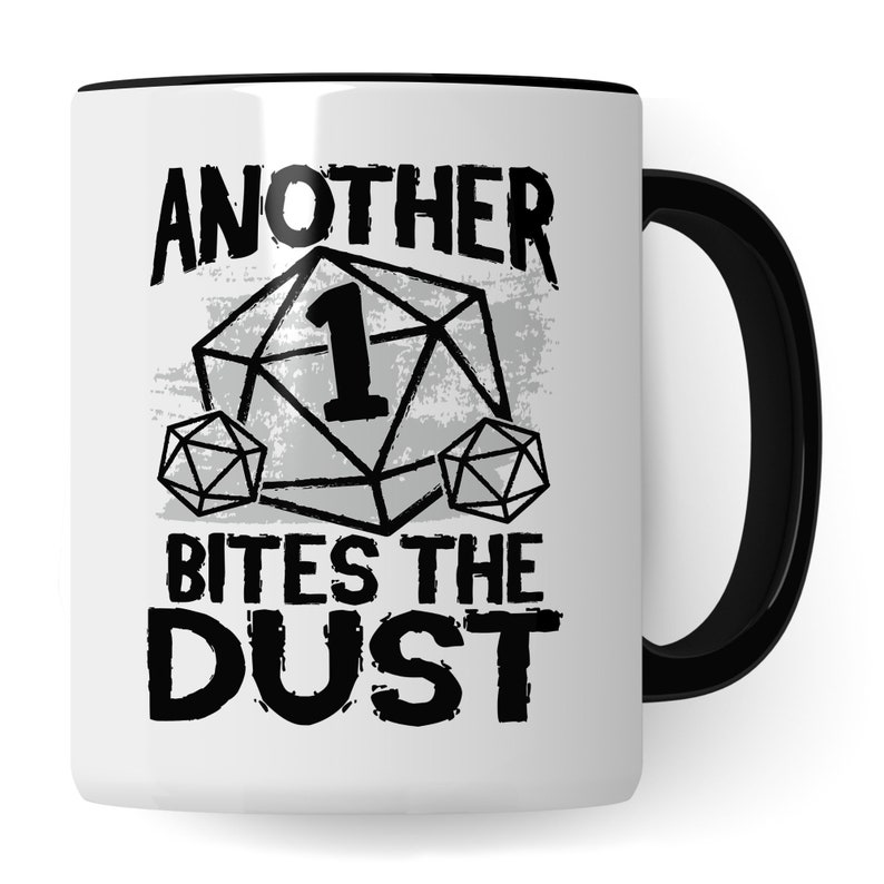 May include: White ceramic mug with a black rim and handle. The mug features a black and white graphic of a dice with the number 1 on it and the text "Another Bites The Dust".