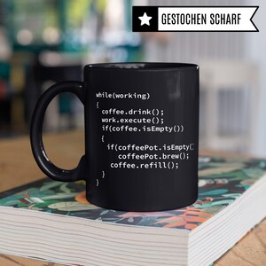 May include: Black coffee mug with white text that reads: "while (working) { coffee.drink(); work.execute(); if(coffee.isEmpty()) { if (coffeePot.isEmpty() coffeePot.brew(); coffee.refill(); } }"