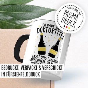 May include: White ceramic mug with a black handle. The mug has a graphic of two champagne bottles with the text "Ich habe einen Doktortitel" and "Lasst uns einfach annehmen, dass ich immer Recht habe". The mug also has a sticker with the text "Pagma Druck" and a German flag.
