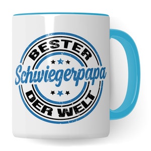 Puede incluir: Taza de cerámica blanca con borde y asa azules. La taza presenta un sello desgastado azul y negro que dice "BESTER SCHWIEGERPAPA DER WELT".