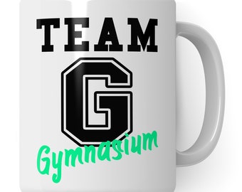 Könnte beinhalten: Weiße Keramiktasse mit einer schwarz-weißen Grafik, auf der in einer stilisierten Schrift "TEAM G Gymnasium" steht. Das "G" ist groß und in einer fetten, blockartigen Schrift.