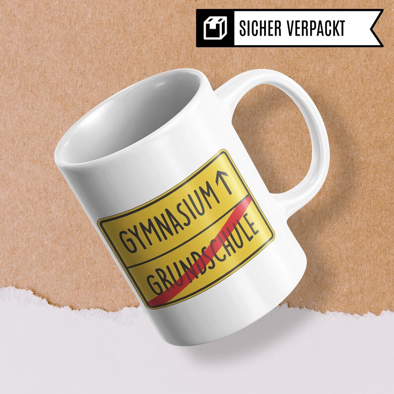 Może przedstawiać: Biały kubek ceramiczny z ż&oacute;łto-czerwonym znakiem drogowym, na kt&oacute;rym widnieje napis "Gymnasium" ze strzałką skierowaną w g&oacute;rę i "Grundschule" z przekreśloną czerwoną linią.