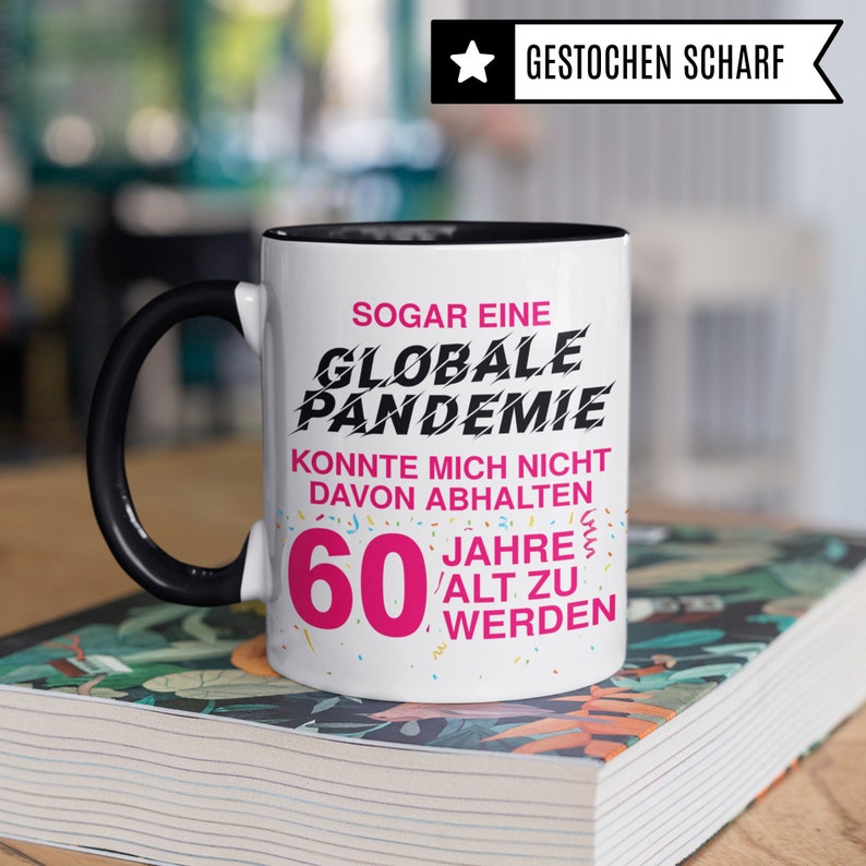May include: White coffee mug with a black rim and handle. The mug has a pink and black graphic that says "Even a global pandemic couldn't stop me from turning 60".