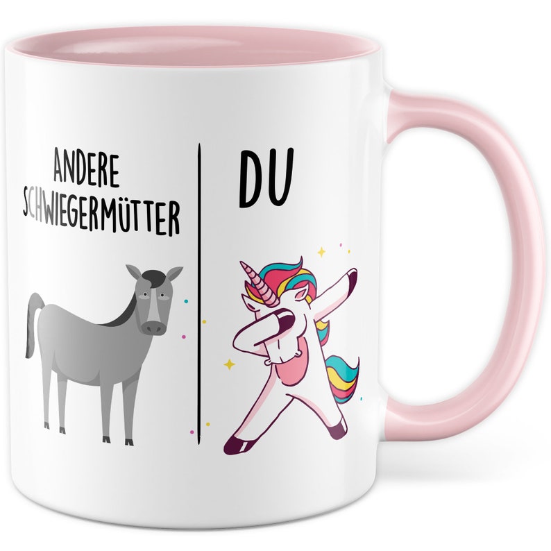 Peut inclure: Une tasse en c&eacute;ramique blanche avec un bord et une poign&eacute;e roses. La tasse pr&eacute;sente un graphique d'un &acirc;ne gris sur le c&ocirc;t&eacute; gauche et une licorne blanche faisant le dab sur le c&ocirc;t&eacute; droit. Le texte "Andere Schwiegerm&uuml;tter" est au-dessus de l'&acirc;ne et "DU" est au-dessus de la licorne.