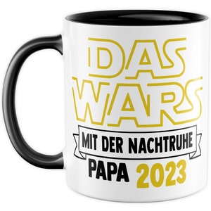 May include: White coffee mug with a black handle and black rim. The mug has a yellow graphic that says "DAS WARS" with a banner that says "MIT DER NACHTRUHE PAPA 2023".