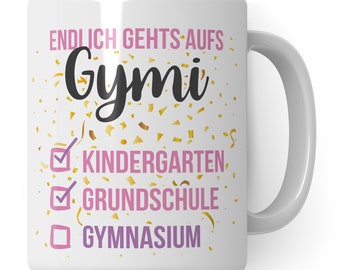 Könnte beinhalten: Weiße Keramik-Kaffeetasse mit einem pinkfarbenen und schwarzen Design. Der Text auf der Tasse lautet "Endlich geht's aufs Gymi" mit einer Checkliste darunter. Die Checkliste enthält "Kindergarten", "Grundschule" und "Gymnasium".