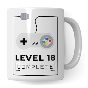 Può includere: Tazza in ceramica bianca con un'illustrazione in bianco e nero di un controller per videogiochi e il testo "LEVEL 18 COMPLETE" in un font pixelato.