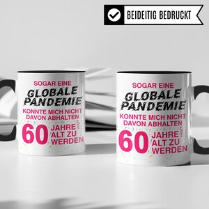 May include: Two white coffee mugs with black handles. Both mugs have a black rim and a pink and black design that says "Even a global pandemic couldn't stop me from turning 60".