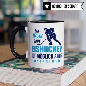Pu&ograve; includere: Tazza da caff&egrave; in ceramica bianca con manico e bordo neri. La tazza presenta una grafica blu e bianca di un giocatore di hockey con un bastone e il testo "Ein Leben Ohne Eishockey Ist M&ouml;glich Aber Sinnlos".