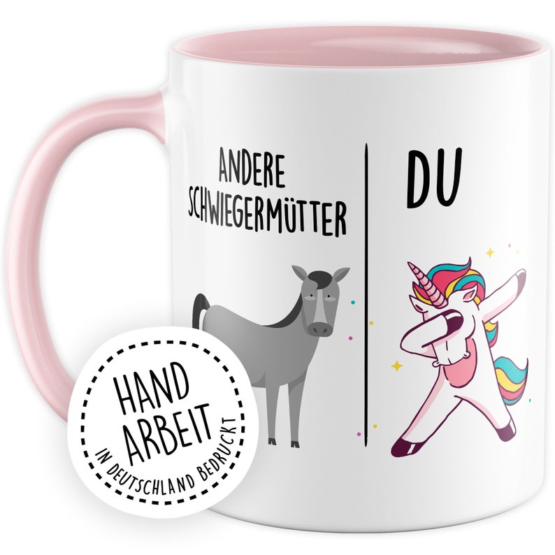 Peut inclure: Mug en c&eacute;ramique blanche avec un bord et une poign&eacute;e roses. Le mug est d&eacute;cor&eacute; d'un motif noir et blanc qui dit "Andere Schwiegerm&uuml;tter" &agrave; gauche et "Du" &agrave; droite. Le motif comprend &eacute;galement un &acirc;ne gris &agrave; gauche et une licorne arc-en-ciel faisant le dab &agrave; droite. Le mug a un autocollant blanc sur le fond qui dit "Handarbeit in Deutschland bedruckt".