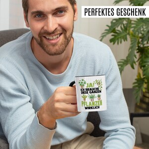 May include: A white ceramic mug with a black handle. The mug has a green and black design with the text "JA! ICH BRAUCHE DIESE GANZEN PFLANZEN WIRKLICH".