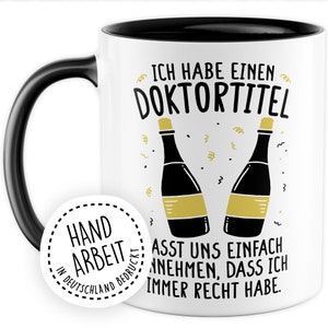May include: White coffee mug with a black rim and handle. The mug has a black and gold design with the text "Ich habe einen Doktortitel" and "Lasst uns einfach annehmen, dass ich immer Recht habe."  The mug also has a sticker on the side that says "Handarbeit in Deutschland Bedruckt".