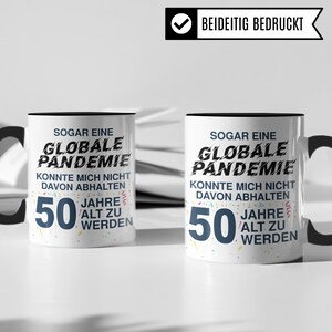 Pu&ograve; includere: Due tazze da caff&egrave; bianche con manici neri e bordi neri. Entrambe le tazze presentano una grafica in bianco e nero con il testo "Sogar eine Globale Pandemie Konnte mich nicht davon abhalten 50 Jahre alt zu werden". Il testo &egrave; circondato da coriandoli colorati.
