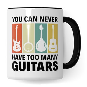 Könnte beinhalten: Weiße Keramik-Kaffeetasse mit schwarzem Rand und Henkel. Die Tasse zeigt ein Retro-Design mit dem Text "You can never have too many guitars" und einer Reihe von vier verschiedenen Gitarrentypen.