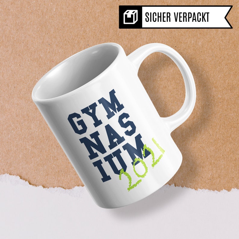 Pu&ograve; includere: Tazza in ceramica bianca con un design blu e verde. La tazza dice "GYMNASIUM 2021" in un font stilizzato.