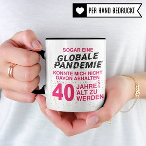 Puede incluir: Taza de cer&aacute;mica blanca con asa negra. La taza tiene un dise&ntilde;o rosa y negro con el texto "SOGAR EINE GLOBALE PANDEMIE KONNTE MICH NICHT DAVON ABHALTEN 40 JAHRE ALT ZU WERDEN".