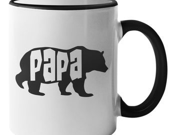 Può includere: Tazza in ceramica bianca con bordo e manico neri. La tazza presenta una silhouette nera di un orso con la parola "papà" scritta in lettere bianche all'interno del corpo dell'orso.
