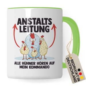 Puede incluir: Taza de cerámica blanca con borde y asa verdes. La taza presenta una ilustración de dibujos animados de una familia de pollos con el texto "Anstalts Leitung" y "Alle Hühner hören auf mein Kommando". Una etiqueta marrón con el texto "Bedruckt in Deutschland" está unida al asa.