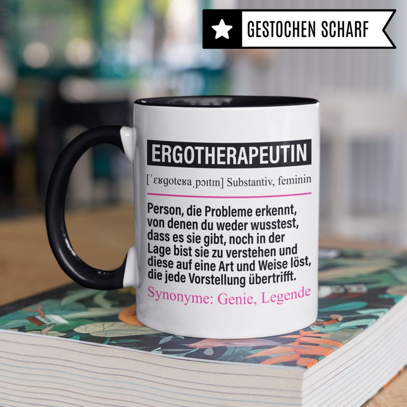 May include: White ceramic mug with a black handle and black rim. The mug features a black and white graphic with the text "ERGOTHERAPEUTIN" and a definition in German. The text "GESTOCHEN SCHARF" is in a star shape at the top of the mug.