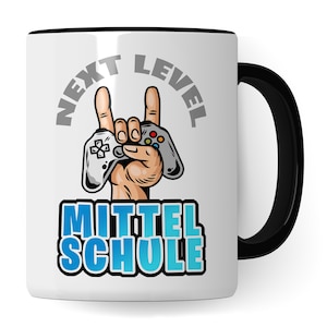 Op de afbeelding: Witte keramische koffiemok met een zwarte handgreep. De mok heeft een afbeelding van een hand die een videogamecontroller vasthoudt met de tekst "NEXT LEVEL MITTELSCHULE" in zwart en blauw.