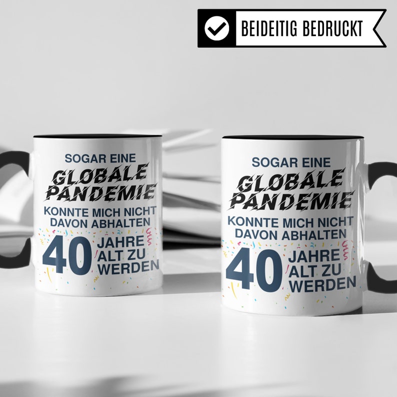 May include: Two white mugs with black handles and black rims. Both mugs have a black and white design with confetti and the text "SOGAR EINE GLOBALE PANDEMIE KONNTE MICH NICHT DAVON ABHALTEN 40 JAHRE ALT ZU WERDEN".