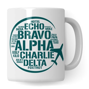 Könnte beinhalten: Eine weiße Keramiktasse mit einem türkisfarbenen Kreisdesign, das das NATO-phonetische Alphabet und eine kleine Flugzeuggrafik zeigt. Der Text lautet "Hotel Echo Bravo Alpha Charlie Delta Foxtrot Whiskey Mike Zulu Papa November Uniform Tango Sierra India Yankee Quebec Oscar Victor X-ray Lima Golf Kilo Juliet Romeo".
