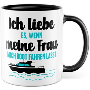 Könnte beinhalten: Weiße Keramiktasse mit schwarzem Rand und Henkel. Die Tasse zeigt eine schwarz-weiße Illustration eines Bootes und den Text "Ich liebe es, wenn meine Frau mich Boot fahren lässt".