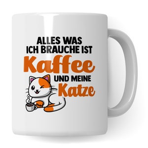May include: White ceramic mug with a cartoon cat and the text "Alles was ich brauche ist Kaffee und meine Katze" in orange and black.