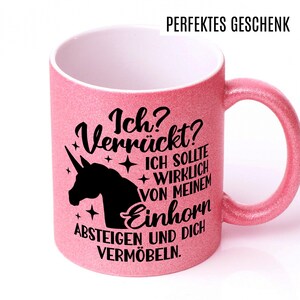 May include: A pink glitter mug with a black unicorn silhouette and the text "Ich? Verr&uuml;ckt? ICH SOLLTE WIRKLICH VON MEINEM Einhorn ABSTEIGEN UND DICH VERM&Ouml;BELN."