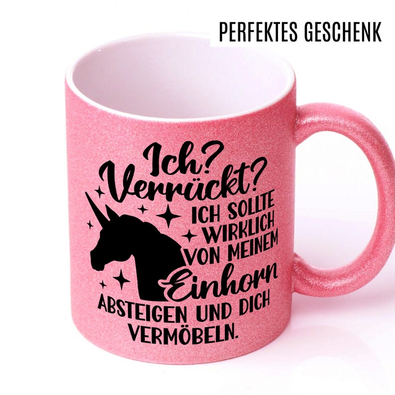 May include: A pink glitter mug with a black unicorn silhouette and the text "Ich? Verr&uuml;ckt? ICH SOLLTE WIRKLICH VON MEINEM Einhorn ABSTEIGEN UND DICH VERM&Ouml;BELN."