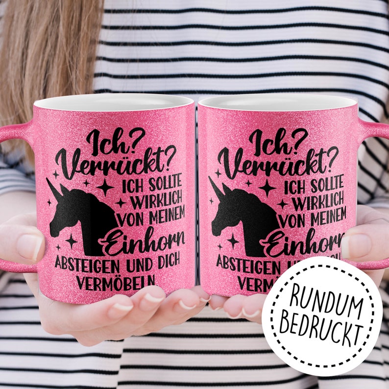 May include: Two pink glitter mugs with black unicorn silhouettes and text that reads "Ich? Verr&uuml;ckt? Ich sollte wirklich von meinem Einhorn absteigen und dich verm&ouml;beln" and "Ich? Verr&uuml;ckt? Ich sollte wirklich von meinem Einhorn absteigen verm" with a white circle around the text "RUNDUM BEDRUCKT".