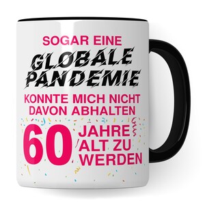 May include: White ceramic mug with a black handle. The mug has a pink and black design with the text "SOGAR EINE GLOBALE PANDEMIE KONNTE MICH NICHT DAVON ABHALTEN 60 JAHRE ALT ZU WERDEN".
